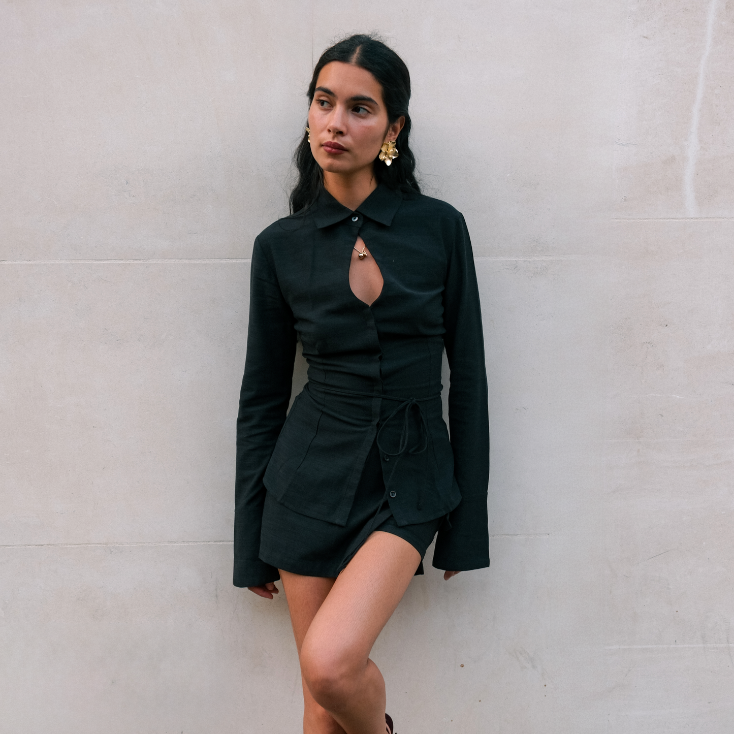 Woman in a black shirt standing against a light-colored wall.